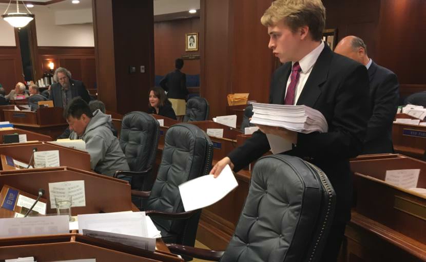 House page Laib Allensworth paces out copies of the capital budget on July 27. Rep. Dean Westlake, D-Kotzebue, reads in the background. (Photo by Andrew Kitchenman/KTOO)