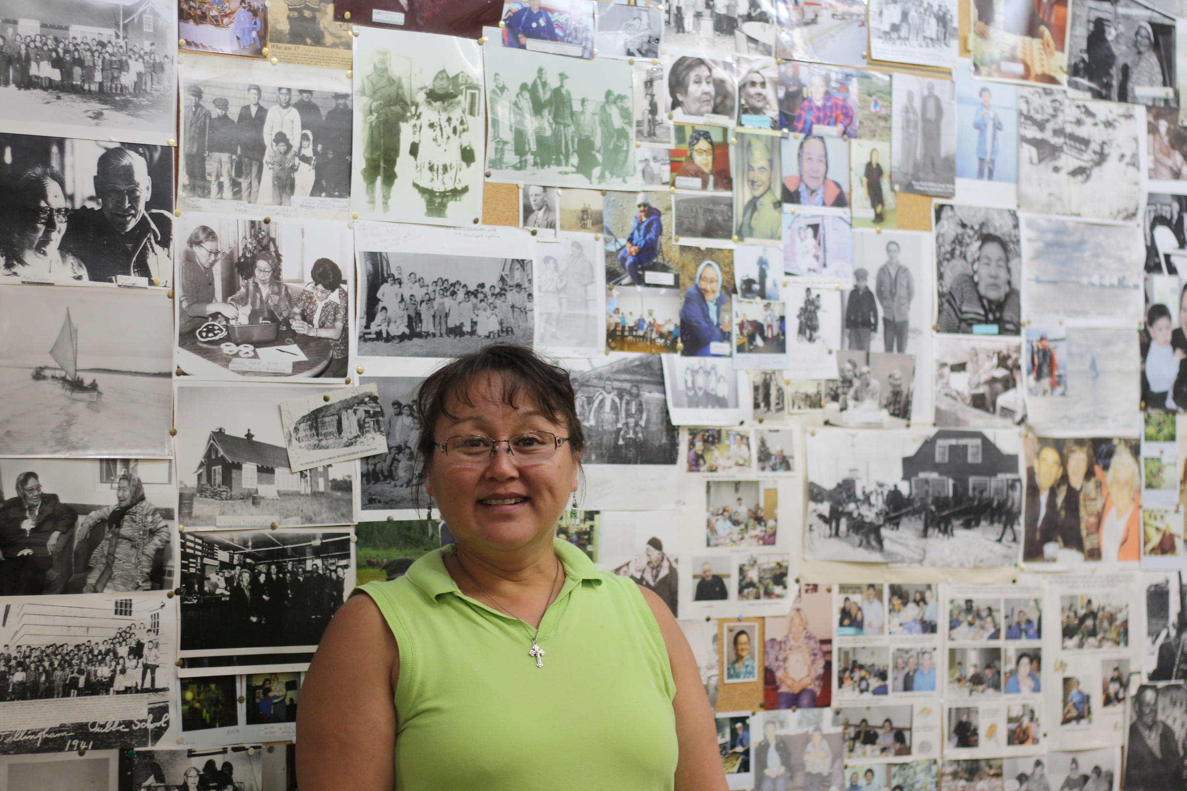 Dillingham Senior Center director Ida Noonkesser stands before a board of memories. Photos of community elders are displayed from years past. Noonkesser was recently recognized for 17 years of service at the center. (Photo by Zoey Laird/KDLG)