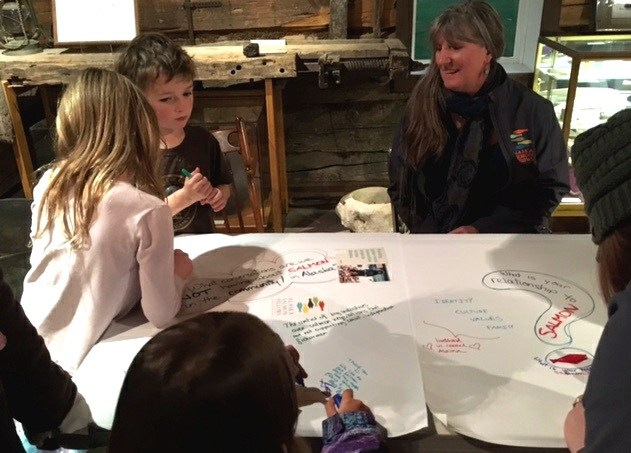Kitty Farnham, right, watches children write responses to fisheries-based questions. (Photo by Kayla Desroches/KMXT)