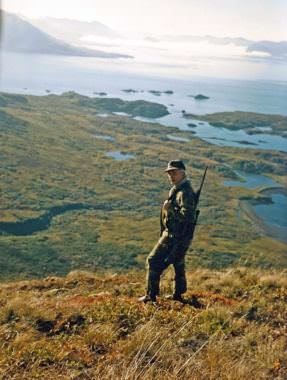 Calvin Fair stands high on “Buck Mountain” north of his group’s hunting camp in a public-use cabin in Chief Cove, which can be seen behind Fair in this October 1986 image. (Photo courtesy Clark Fair)