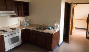 A small kitchenette in the corner of an apartment with a full sized refrigerator, oven, and sink