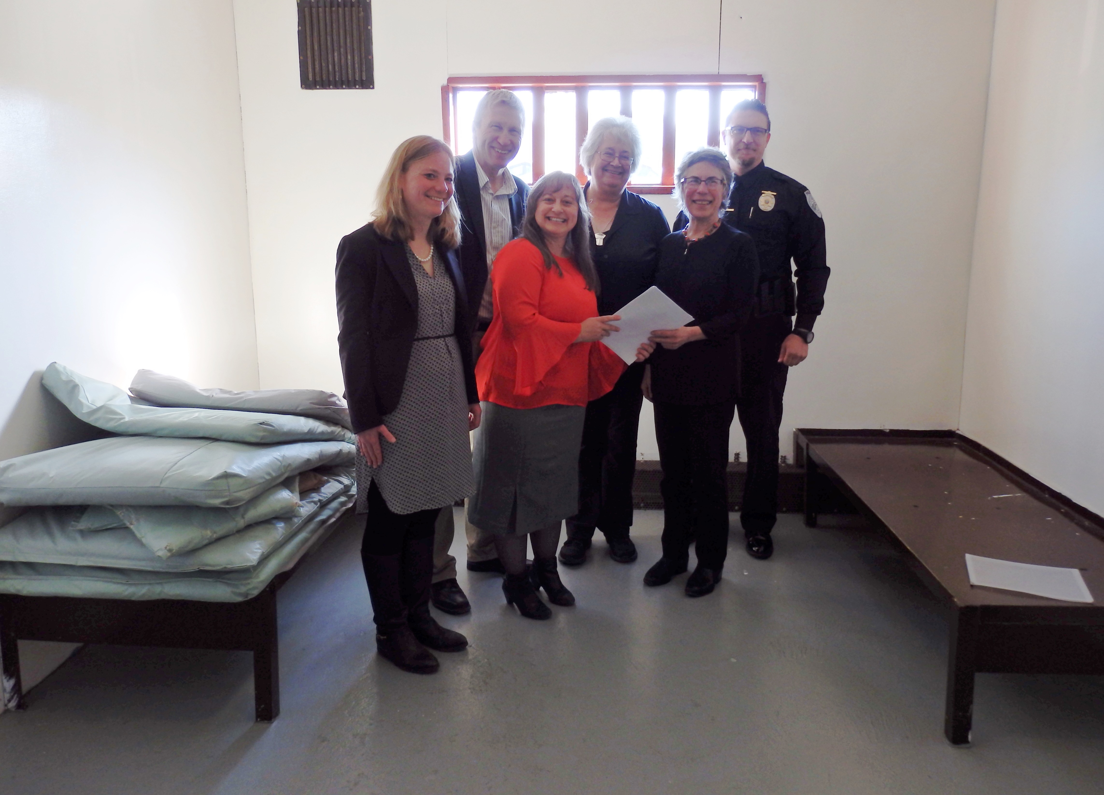 Heather Parker with Gov. Walker’s office, DOC Commissioner Dean Williams, Pretrial Director Geri Fox, Haines Mayor Jan Hill, Haines Borough Manager Debra Schnabel and Haines Police Chief Heath Scott pose in a Haines jail cell with a revised community jails contract. (Photo by Emily Files/KHNS)