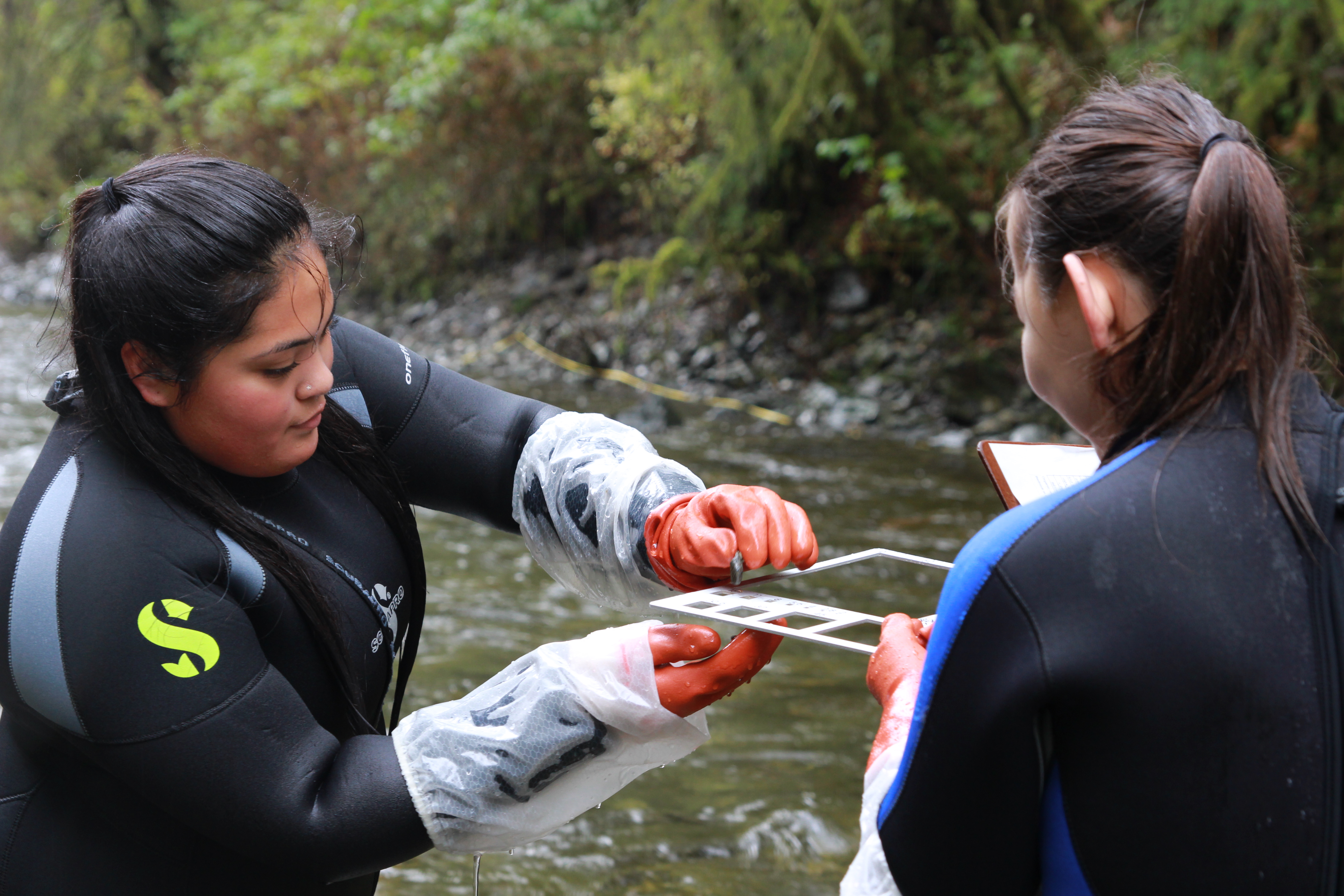 Mt. Edgecumbe High School students Kori Itta-Thomas and Katelynn Johns measure rocks from the bed of Indian River. (Photo by KCAW)