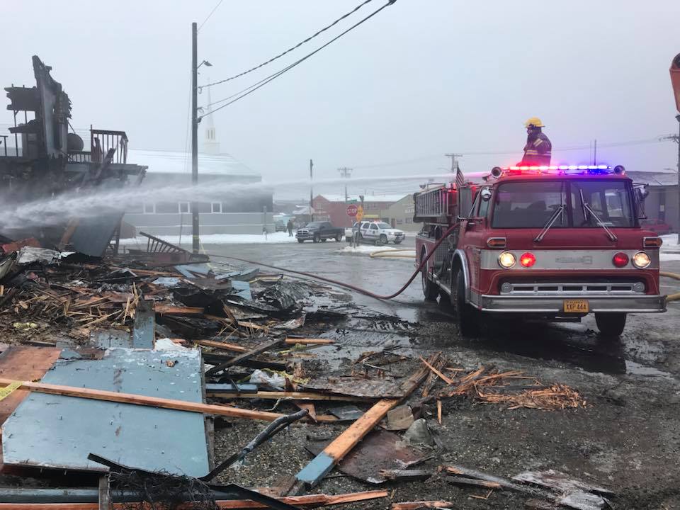Nome’s volunteer firefighters spray what remains of the Polaris Hotel earlier Thursday to cool off the site before investigators with the State Fire Marshal’s Office arrive. (Photo courtesy John Handeland)