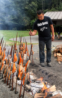 At the 55th Annual Yurok Salmon Festival, Oscar Gensaw cooks salmon the traditional way, on redwood skewers around a fire pit. This year, though, the tribe had to buy salmon from Alaska. (Photo by Lisa Morehouse/KQED)