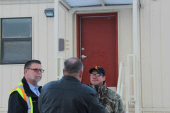 From left, Darryl Parks, chief of operations in civil engineering at JBER; Bob Sherrill of the Defense Logistics Agency; and Newtok Tribal Administrator Andrew John stand in front of one of the barracks units. (Photo by Rachel Waldholz/Alaska's Energy Desk)