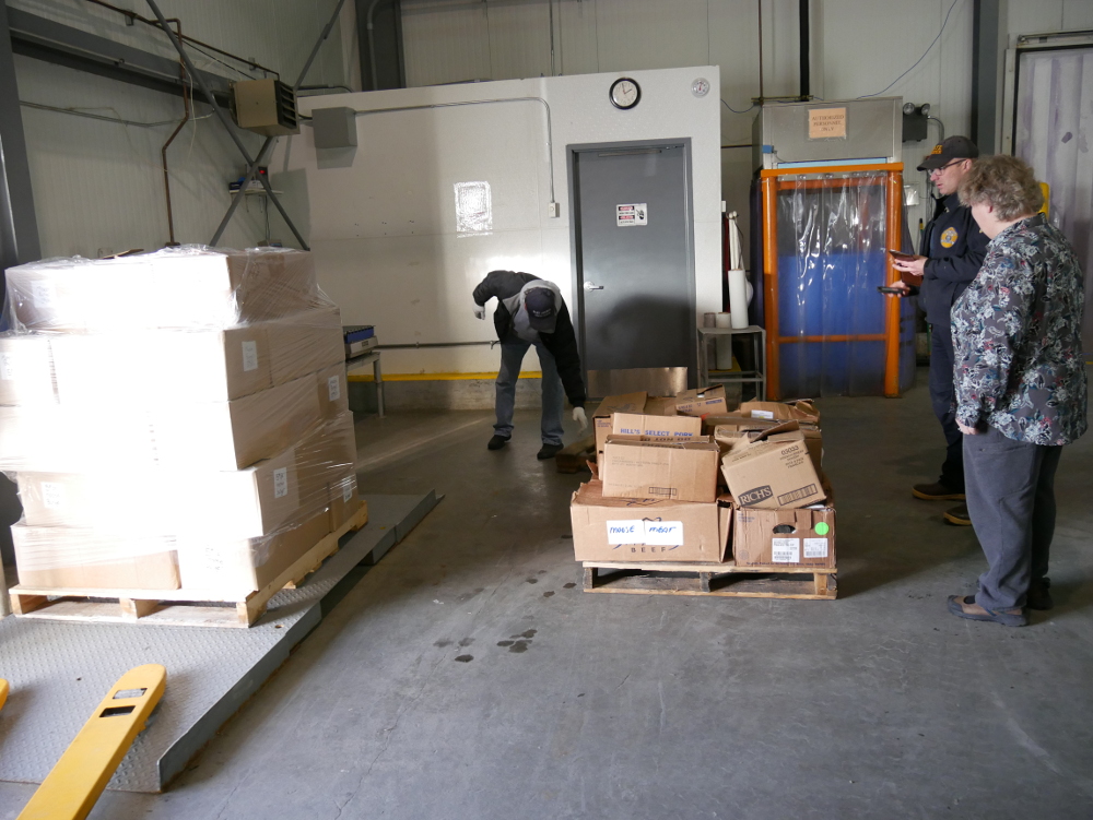 Petersburg community cold storage manager Marv King, wildlife trooper Cody Litster and Salvation Army major Loni Upshaw prepare two pallets of moose meat for distribution at the cold storage Thursday, December 7, 2017. (Photo by Joe Viechnicki/KFSK)