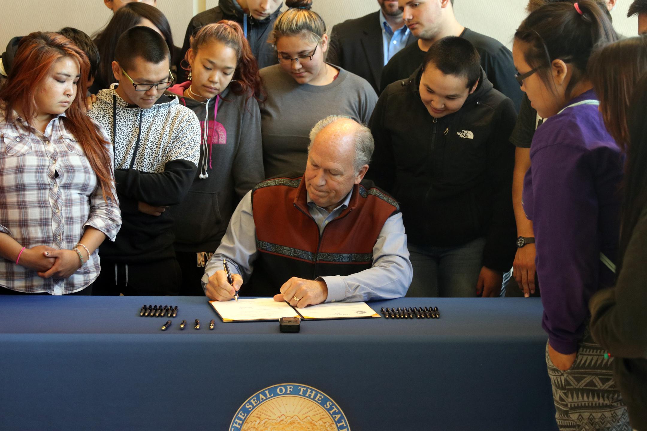 Gov. Bill Walker signs House Bill 141 at Bethel's Yuut Elitnaurviat surrounded by high school students from the Kuskokwim Learning Academy on August 29, 2017. The governor has selected Rep. Fansler's replacement remarkably quickly. (Photo by Dean Swope/KYUK)