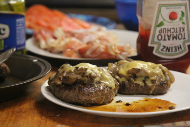 Dennis Davis’s musk ox burgers, topped with Swiss cheese, sautéed onions and mushrooms, along with freshly sliced prosciutto and a home-made aioli. Or ketchup. (Photo by Zachariah Hughes/Alaska Public Media)
