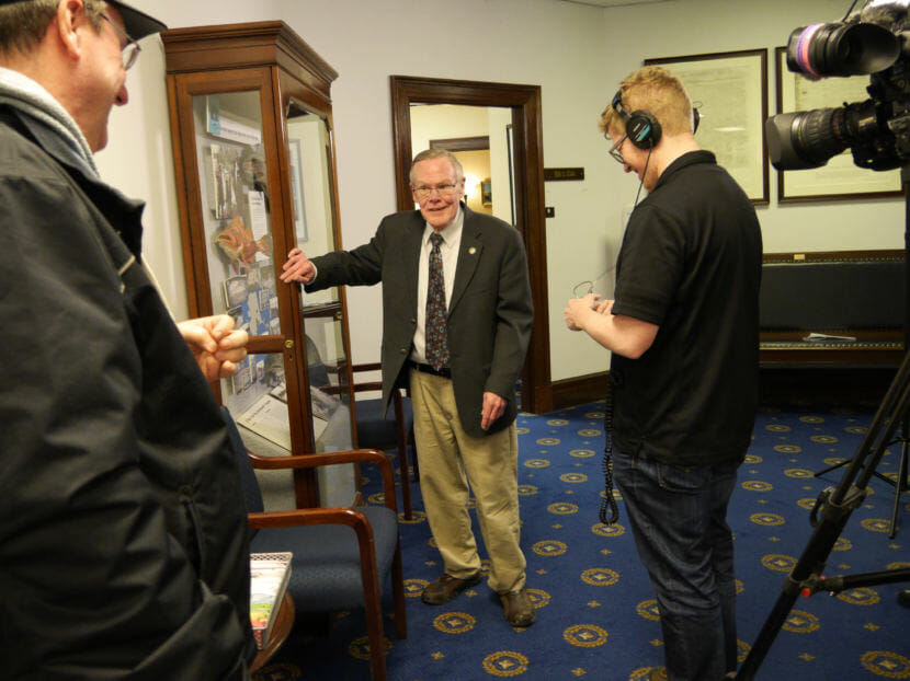 Sen. Dennis Egan hangs on to a display cabinet in the Capitol for support while chatting with a KTVA television crew after doing an interview on Feb. 8, 2018. Egan suffers from multiple sclerosis and severe vertigo, to which he attributed his decision not to run for re-election following the end of his term. Also pictured: KTVA reporter Steve Quinn, left, and camera operator Ken Kulovany. (Photo by Skip Gray/360 North)