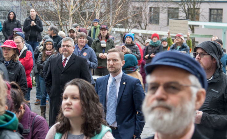 Alaska State Reps. Jason Grenn, center, and Paul Seaton, foreground, watch a student walkout protest at the Alaska State Capitol building in Juneau on Wednesday, March 14, 2018.