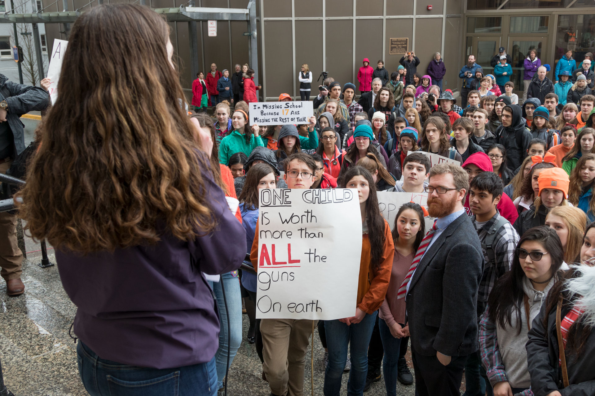 Katie McKenna speaks on the steps of the Alaska State Capitol building in Juneau at a student walkout protest on Wednesday, March 14, 2018. Students and Juneau Rep. Justin Parish, wearing the coat and tie, listen.
