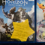 A video game box with a large yellow star stuck on the front. The star is labeled "Asexual female protagonist, trans man NPC, widely diverse cast of POC NPCs"