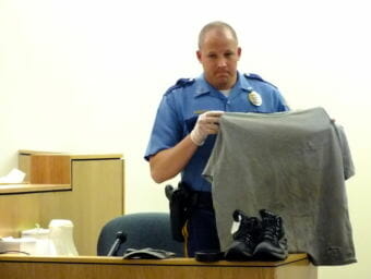 Alaska State Trooper Ryan Anderson holds up Mark DeSimone's shirt for the jury on May 4, 2018. The shirt, along with DeSimone's coat, cap, belt, jeans and boots, were seized after the shooting of Tony Rosales in Excursion Inlet in May 2016. A sample taken from DeSimone's shirt matched Rosales' DNA.