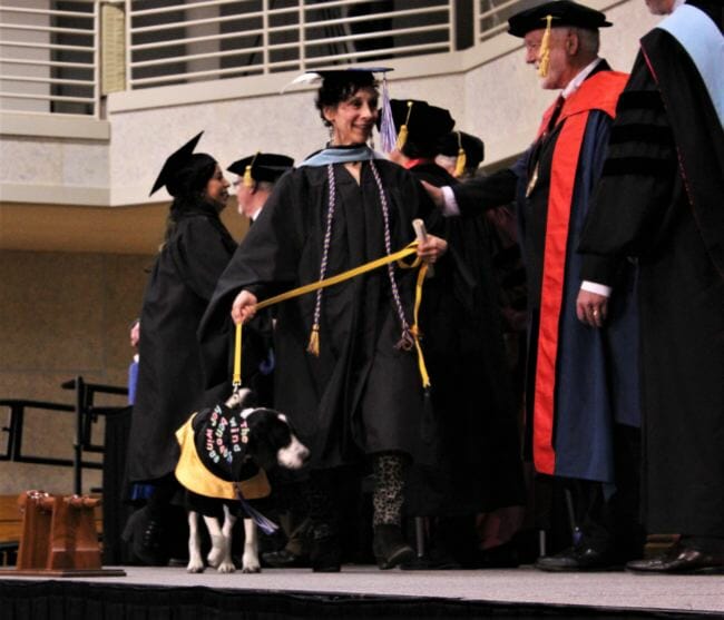UAS graduate Barbara Van Flein walks across the stage with her service dog, Capone. (Photo by Adelyn Baxter/KTOO)