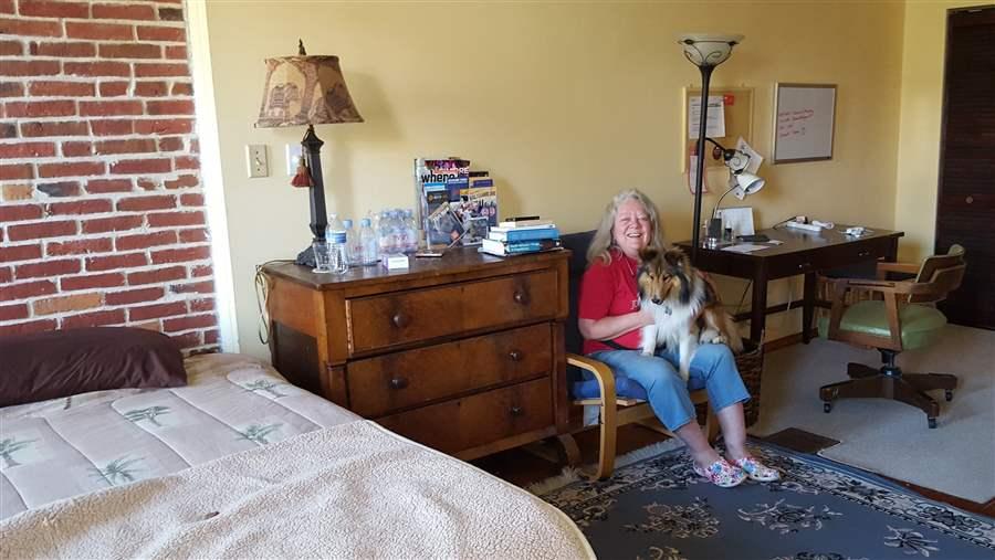 Baltimore resident Jeannette Belliveau, who rents a couple of rooms in her historic townhouse to short-term guests, sits with her dog, Copper, in one of the guest suites. States are having a hard time regulating the short-term rental industry. (Photo by Pew Charitable Trusts)