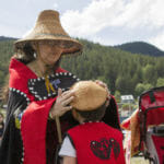 A woman helps a child with his hat Tuesday, June 5, 2018, while waiting for the canoes at Douglas Harbor.