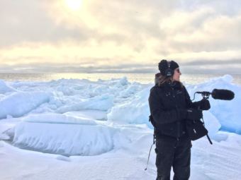 Ravenna Koenig of Alaska's Energy Desk/KTOO stands on the lead edge of the sea ice while recording sound for a story about Arctic Field School. (Photo courtesy of Lindsay Cameron)