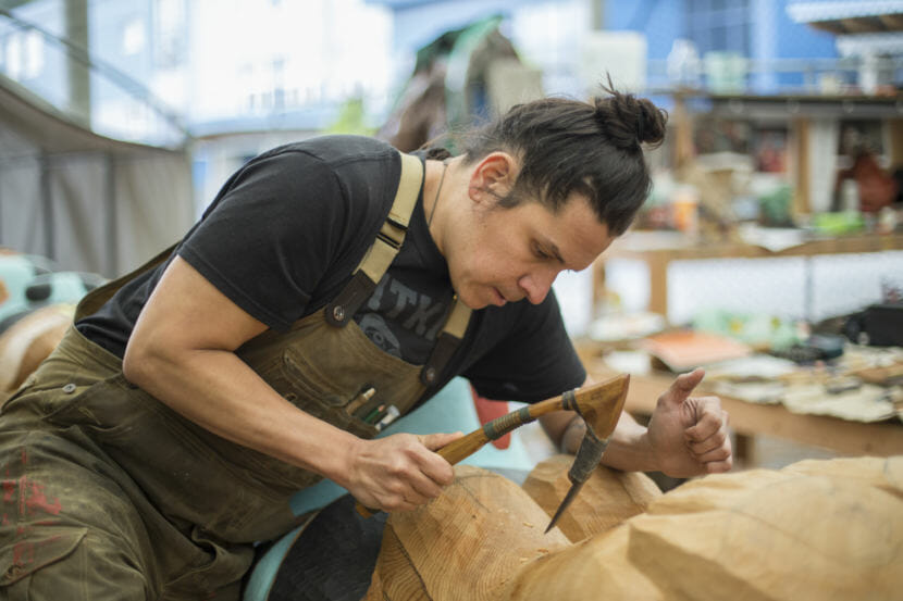 A carver uses an adze on a totem pole