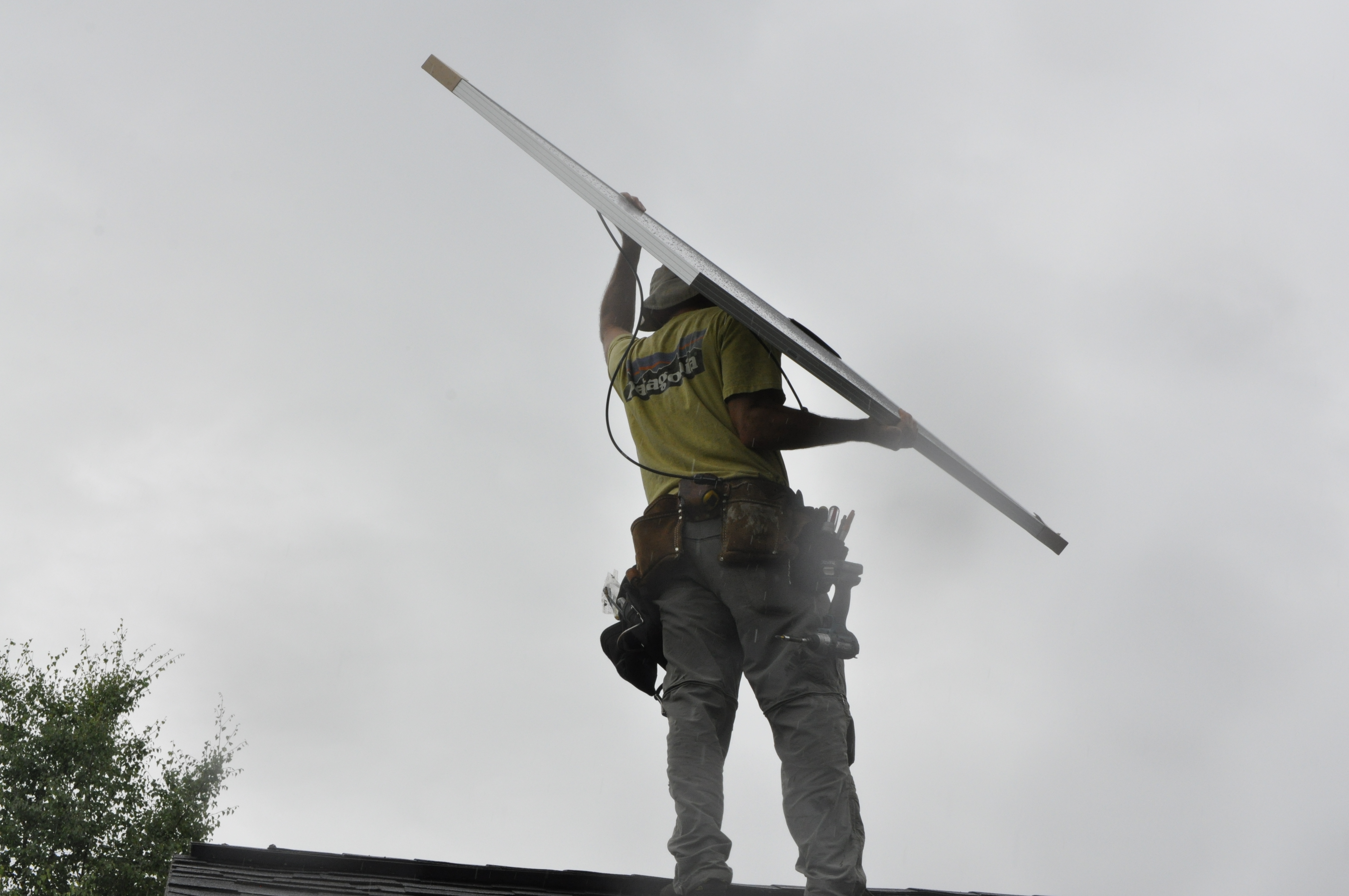 Anchorage Solar employee Tim Remick hoists a solar panel over his head before installing it on Solarize Anchorage participant Lisa Pekar’s roof. The program saved participants around 10 percent on solar panel installations. (Photo by Erin McKinstry, Alaska Public Media)