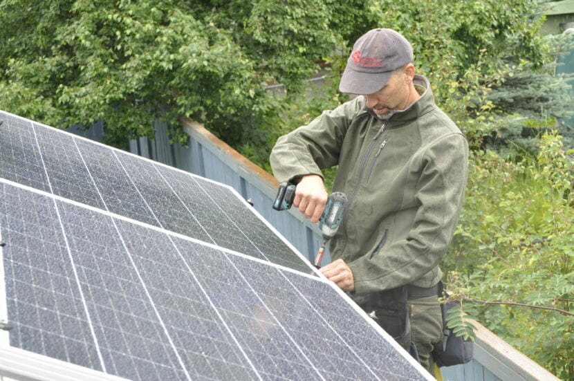 Anchorage Solar owner Ben May secures a solar panel on Lisa Pekar’s garage roof. He said business has increased almost eight-fold since he opened in 2016. “You caught me mid-way through a costume change,” he said. “I wear many hats.” (Photo by Erin McKinstry/Alaska Public Media)