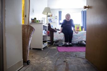 Terry Baker sits on her bed in an apartment recently stripped of wet carpet on July 12, 2018, at the Mendenhall Tower apartments in Juneau. Baker's apartment is near one that caught fire and damaged the building extensively.