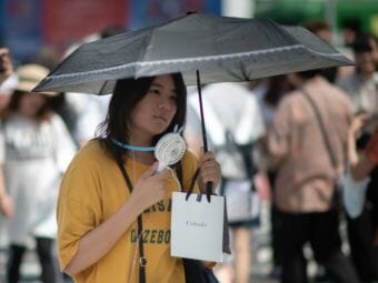 A woman uses a portable fan to cool herself in Tokyo on Tuesday as Japan suffers from a heat wave. Scientists say extreme weather events will likely happen more often as the planet gets warmer. (Photo by Martin Bureau/AFP/Getty Images)