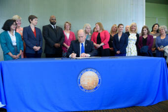 Gov. Bill Walker signs Senate Bill 105 into law during an Anchorage Chamber of Commerce luncheon at the Dena'ina center in Anchorage on Aug. 6, 2018. The bill promotes competition for health care services by requiring providers to post prices for their most common health care services. Also pictured are Rep. Ivy Sponholz, third from the left, Sen. David Wilson, fourth from left, first lady Donna Walker directly behind the governor, and Rep. Geran Tarr to her left.