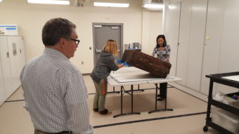 Sealaska Heritage Institute heritage director Chuck Smythe watches Monday, August 14, 2018, as collections manager Heather McClain and summer archives intern Miranda Worl set the bentwood box drum down to return to the collections. (Photo by Tripp J Crouse/KTOO)