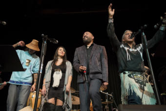 Four people dance and sing into microphones. Vocalists Nahaan, Sondra Segundo, Stephen Blanchett and Gene Tagaban sing with Khu.éex' at Centennial Hall on Monday, January 28, 2019. The Seattle-based band played the 16th Annual World Music Celebration in Anchorage before their Juneau concert. (Photo by Annie Bartholomew/KTOO)