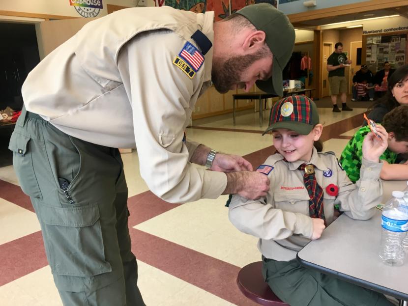 Kelsie Powers' father -- and assistant den leader -- attaches the new badges she earned to her Scout uniform at a pack meeting on April 20, 2019. (Photo by Zoe Grueskin/KTOO)