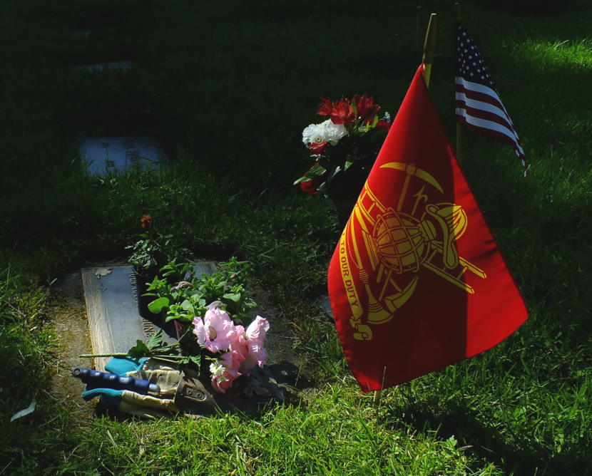 Jack Gould's daughter-in-law sets aside her grave tending tools to watch the Memorial Day service at Evergreen Cemetery on May 27, 2019. The red and yellow flag signifies that the deceased was a veteran of the local fire department.