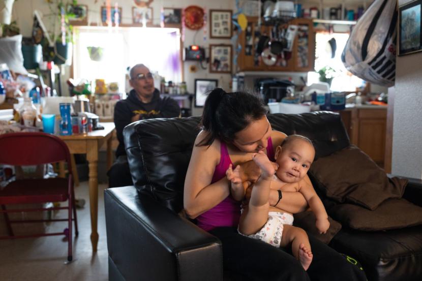Katelynn Reed, 22, with her son Abram Reed-Jordan, then 7 months, in her family's home. Behind is her father, Jack Reed. Katelynn's mother, Annie Reed, is often the town's only cop.