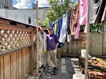 Martha and Jim Stey stand beneath the Purple Air air quality sensor installed by DEC in their backyard. They nicknamed the sensor Jon, after this late friend Jon Sandstedt. (Photo by Adelyn Baxter/KTOO)