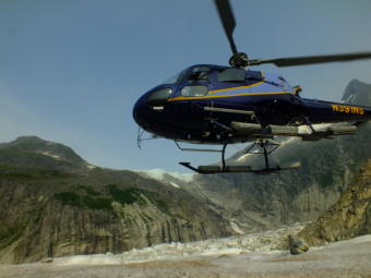 A helicopter arrives to pick up scientists left on the Mendenhall Glacier for the study of nearby Suicide Basin (background), the source of jökulhlaups that have flooded Mendenhall Lake and Mendenhall River in recent years. Water from Suicide Basin Falls (located just under the lips of ice on the ridge) accumulates in the basin and is trapped by Mendenhall Glacier until a glacial dam release starts.