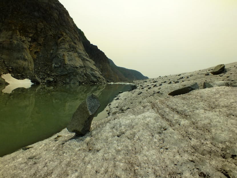 This dog-sized piece of granite rock, called a glacial erratic, stands naturally balanced on the edge of Mendenhall Glacier. The adjacent pool of water has spilled over from an ice dam that is holding back most of the water in Suicide Basin.