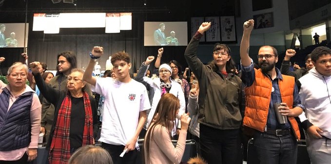 Protesters stand with their back to the stage during Gov. Mike Dunleavy’s speech at the AFN Convention in Fairbanks on Thursday, Oct. 17, 2019.