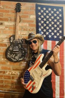 Johnny Solinger poses with a guitar signed by Ted Nugent at the Pacific Yard House in Conroe, Texas. The guitar on the wall is one of eight he owns that he and other rock stars signed that he intends to auction off for charity, including one to help Alaska veterans.