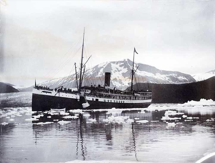 Steamer Queen taking on ice in Takou Inlet sometime between 1896 and 1913. Note the people standing on the deck and the net hauling up a piece of ice with the glacier in background. (P95-040 Alaska State Library - WLR Photo Collection)