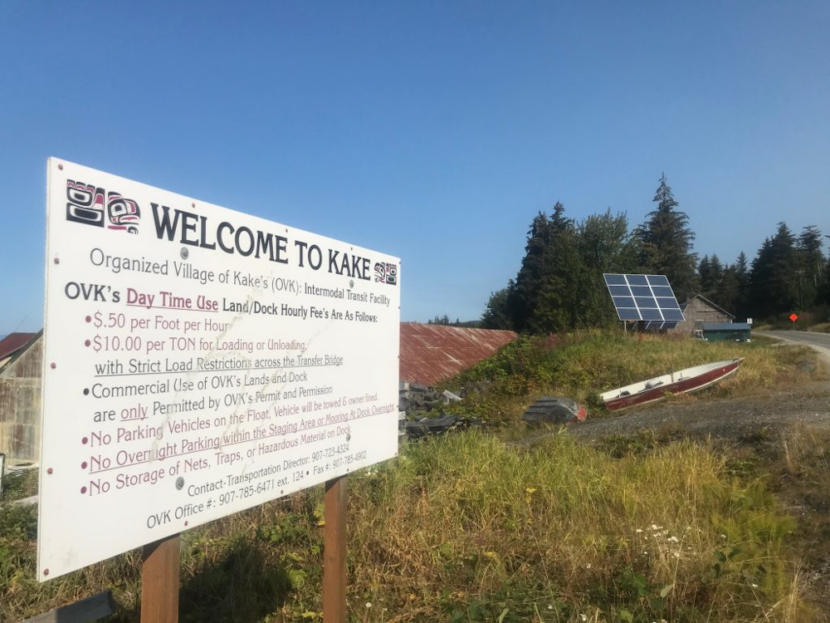 A sign that says "Welcome to Kake" in the foreground, with a solar panel in the background.