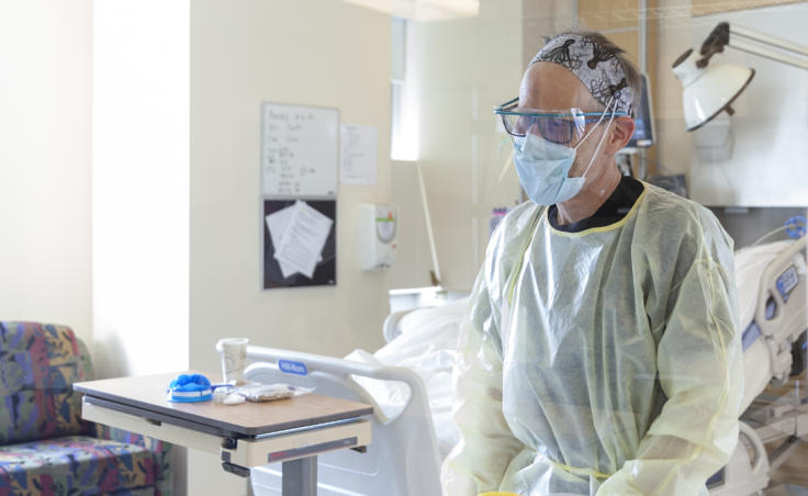 A healthcare provider, wearing several types of personal protective equipment that is being tracked by the State of Alaska, provides care on April 7, 2020, for a woman hospitalized in an isolation room in the critical care unit of Bartlett Hospital, in Juneau, Alaska. on (Photo by Rashah McChesney/KTOO)