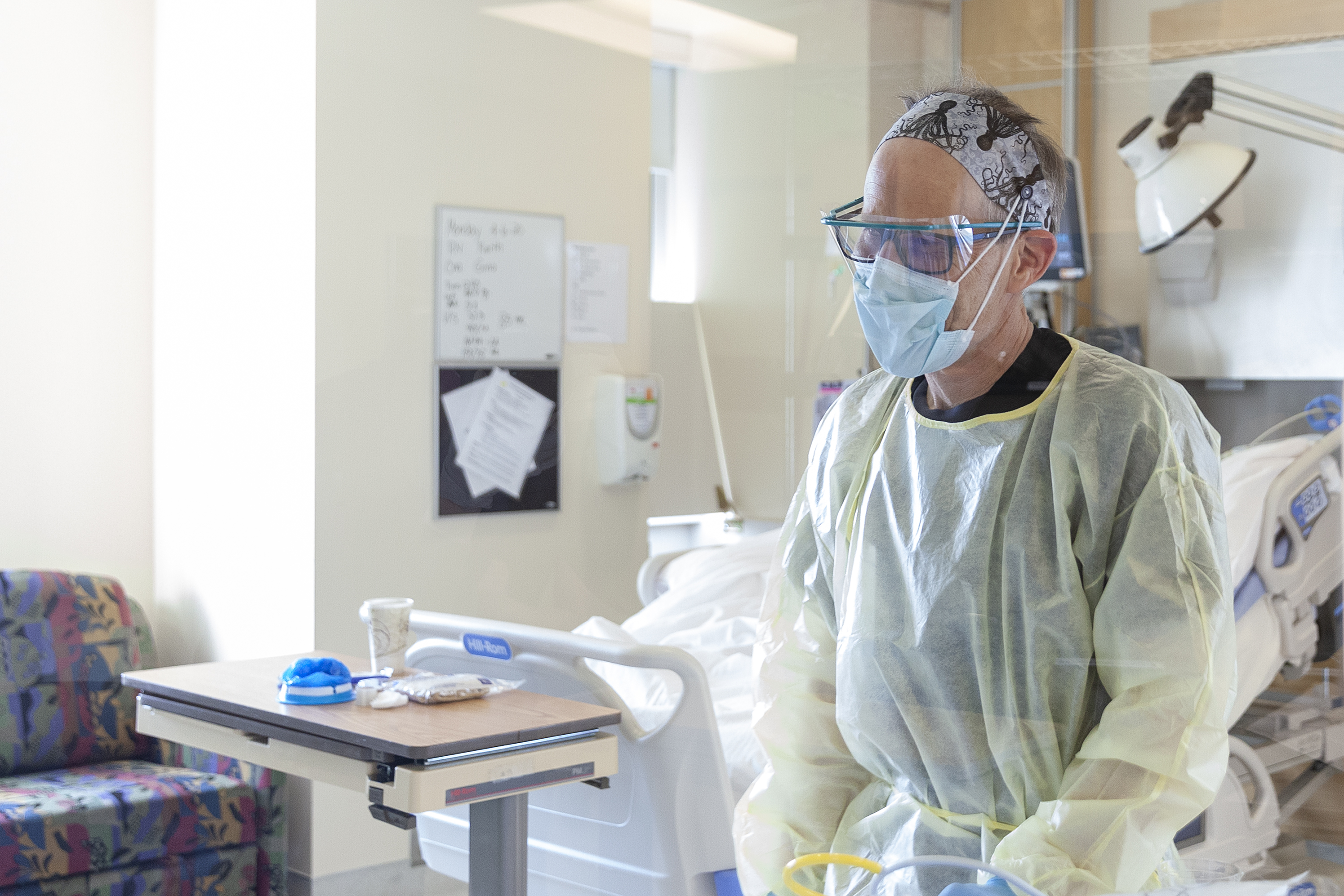 A healthcare provider, wearing several types of personal protective equipment that is being tracked by the State of Alaska, provides care on April 7, 2020, for a woman hospitalized in an isolation room in the critical care unit of Bartlett Hospital, in Juneau, Alaska. on (Photo by Rashah McChesney/KTOO)