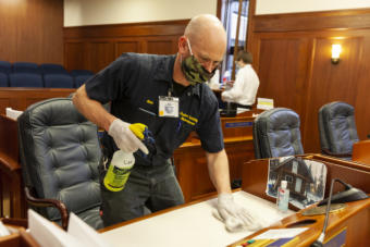 Nathan Paris cleans the desks on the floor of state House after legislators held a session on Monday, May 18, 2020, in Juneau, Alaska. (Photo by Rashah McChesney/KTOO)