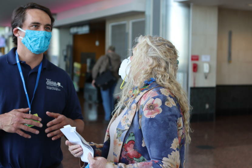 Lisa Starr, a visitor from Kansas, talks to Jeremy Zidek, a spokesman for the state Department of Homeland Security and Emergency Management. Starr had questions about what to do with her declaration form and proof that she had tested negative for the coronavirus within the past three days. Starr is visiting her newborn grandson. She said it took her days to find a testing site with a quick-enough turnaround time. Photographed at the Ted Stevens Anchorage International Airport on Friday, June 5, 2020. (Tegan Hanlon/Alaska Public Media)