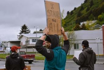 Elinore Millstein holds a sign reading “I stand for all” at the intersection of Rezanof Dr. and Mill Bay Rd. on Sunday. (Photo by Kavitha George/KMXT)