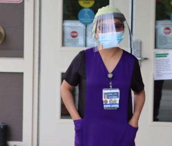 A nurse with a face shield standing outside Providence Transitional Care Center in Anchorage
