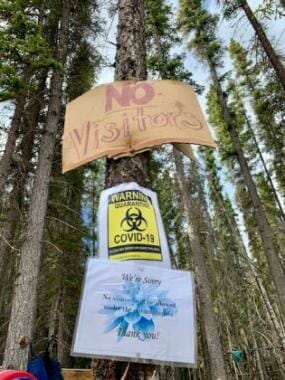 Signs on a tree at a fish camp saying no visitors are allowed due to COVID-19.