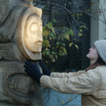 12. Ellen Carlee directs the installation of the refurbished Harnessing the Atom totem next to the Juneau City Museum as a beam of light from the setting sun illuminates the sun figure in the totem. It was carved by master Tlingit carver Amos Wallace.