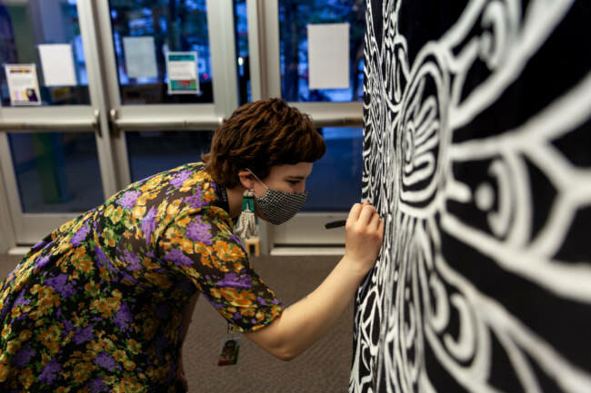 Yeeskanaalx Tláa, cultural specialist at Sayeik Gastineau Community School puts the finishing touches on an eagle formline background she made for students who are attending in-person classes on Thursday, Jan. 14, 2020, in Juneau, Alaska. (Photo by Rashah McChesney/KTOO)