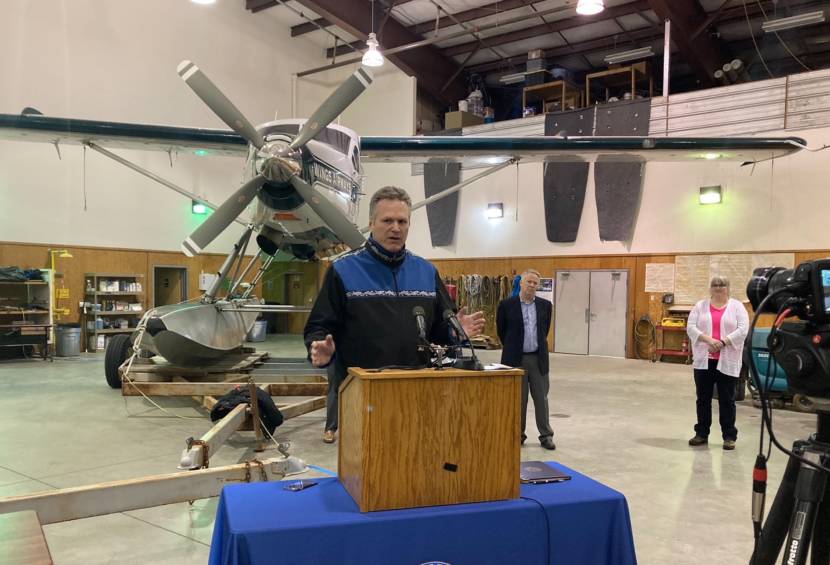 Alaska Gov. Mike Dunleavy speaks about his hopes for holding a summer cruise season this year in a news conference in the hangar of Wings Airways in Juneau, Alaska, on April 9, 2021. Holland America executive Ralph Samuels and Juneau Mayor Beth Weldon are behind Dunleavy. (Photo by Andrew Kitchenman/KTOO and Alaska Public Media)